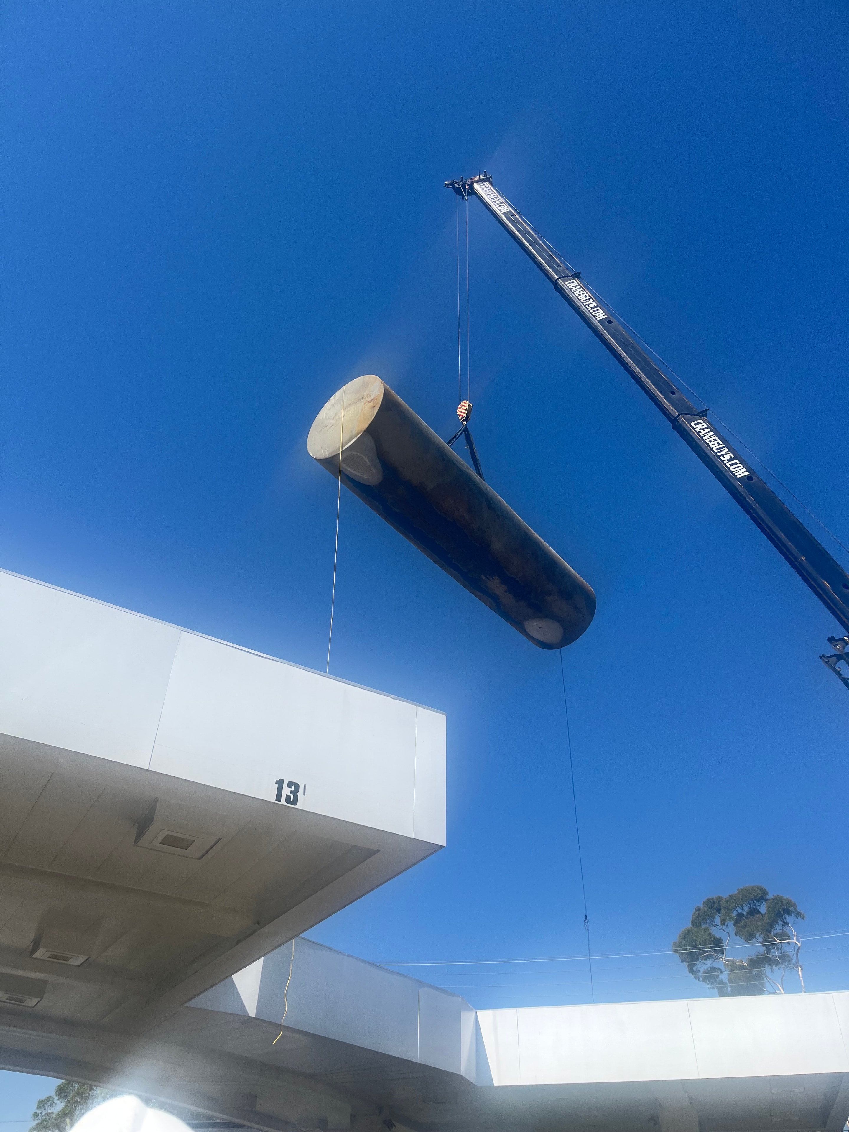 Crane lifting a large pipe beside a modern building